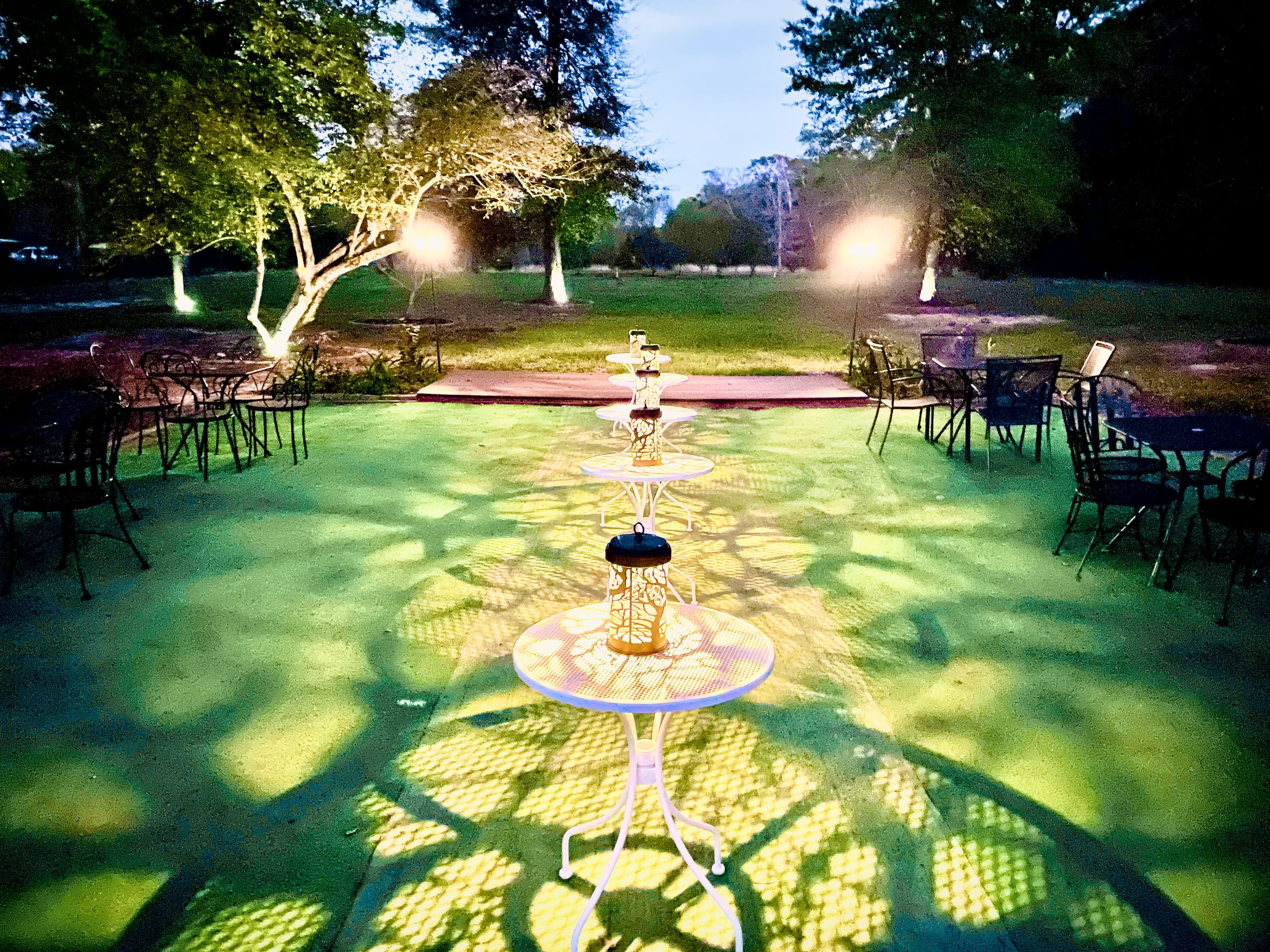 Lounge tables around a tiered white stand, patterned light across the lawn at night