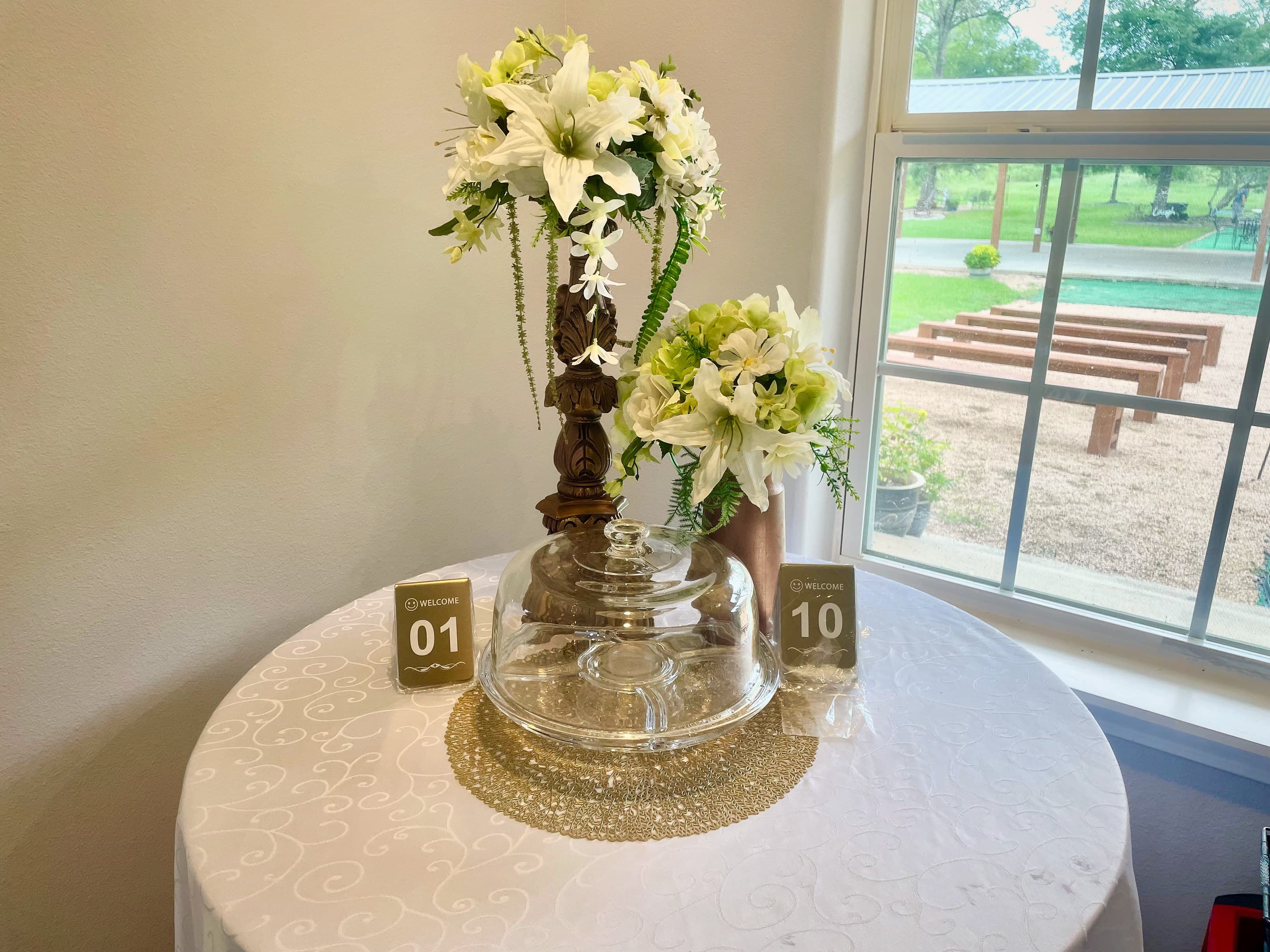 A tall lily centrepiece on a round table beside a window overlooking the ceremony lawn