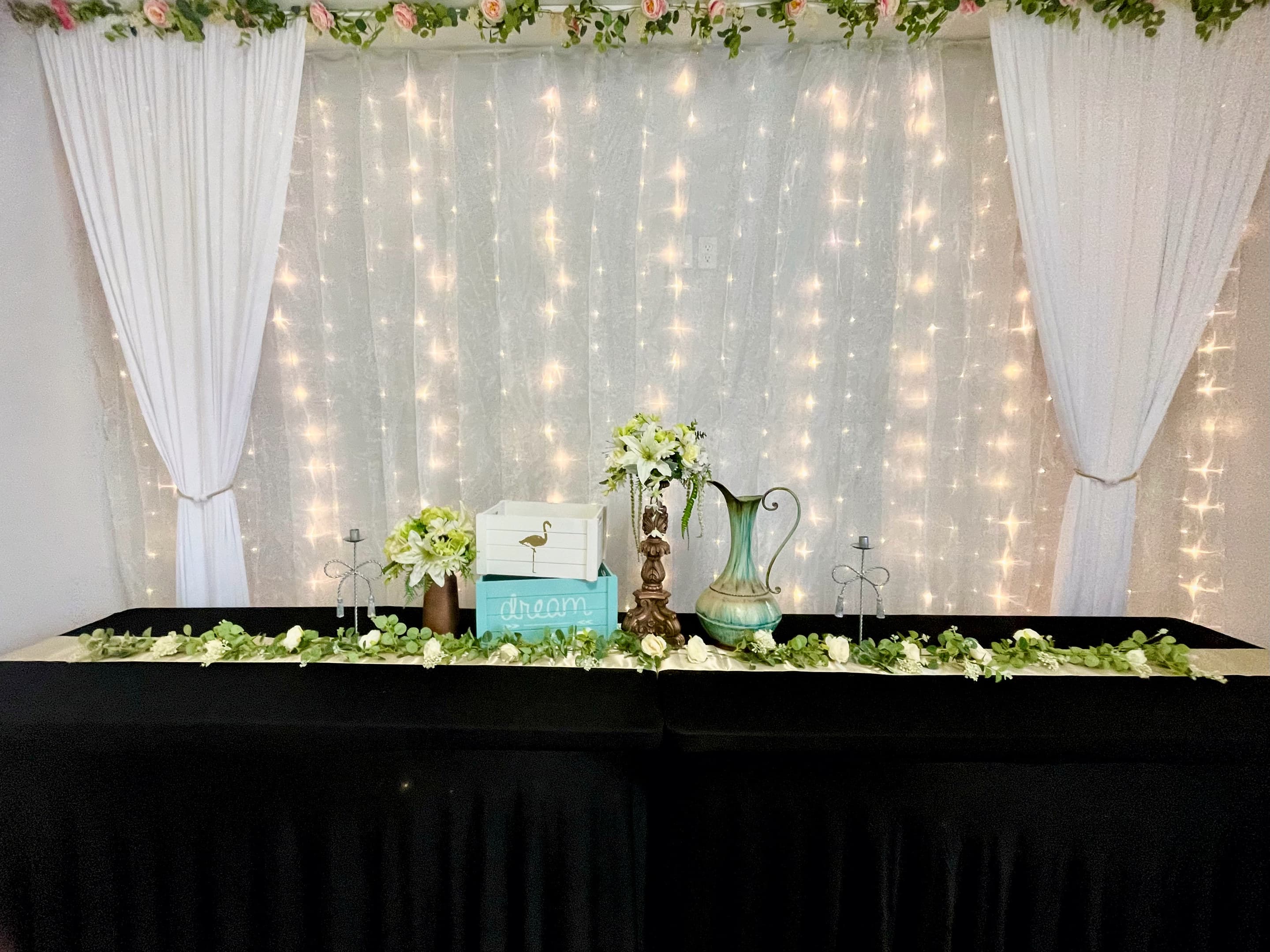 A curtain of fairy lights and sheer drapery behind a table of white florals in the great hall