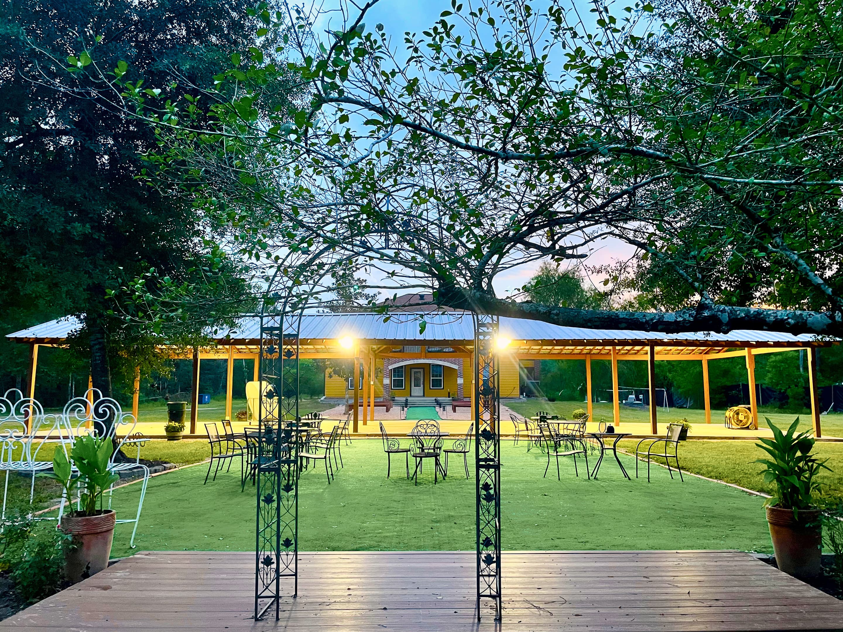 A wrought-iron arbor on the deck, the pavilion glowing through the trees at dusk