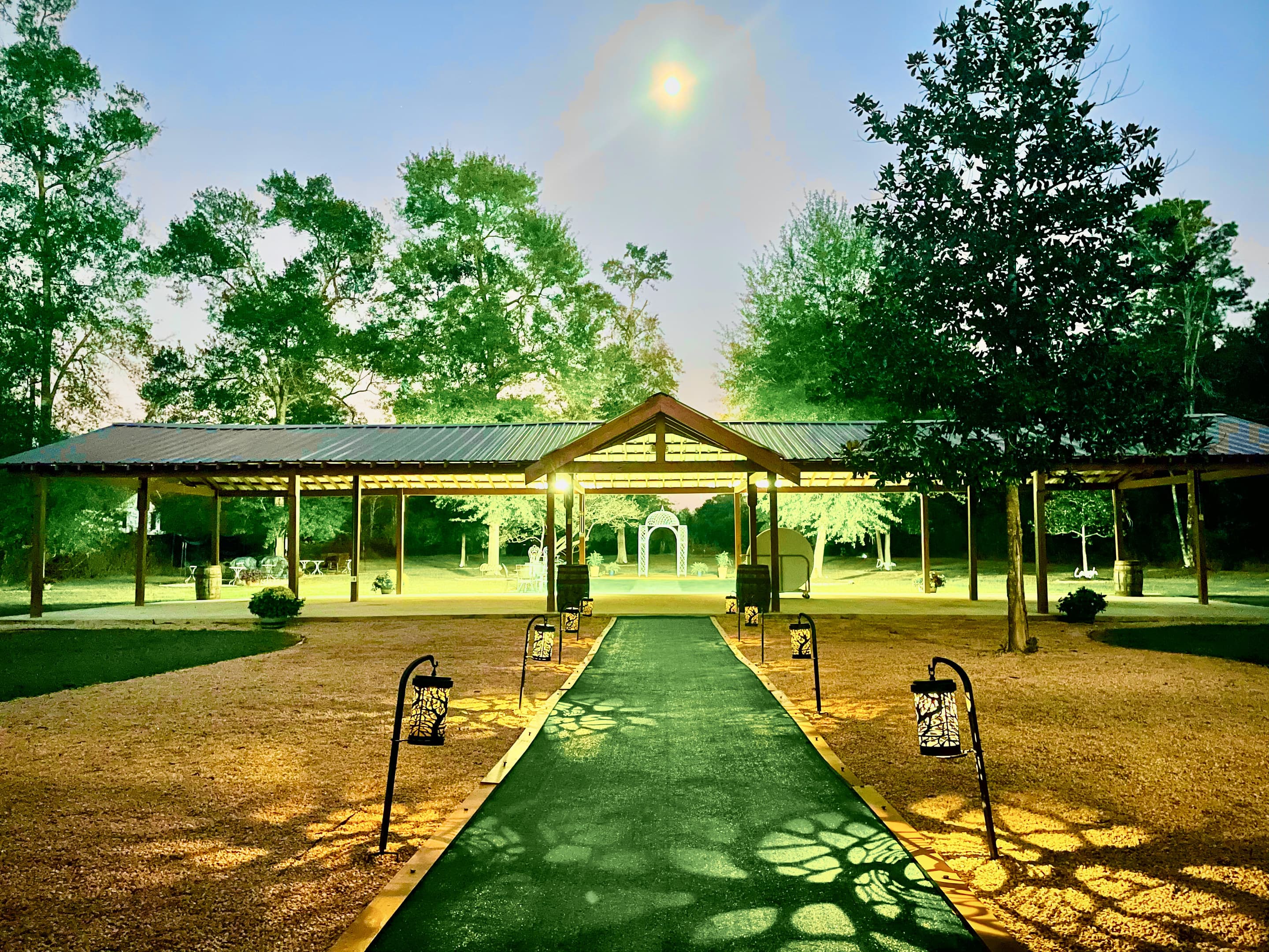 Lantern light patterning the aisle toward the pavilion as evening falls