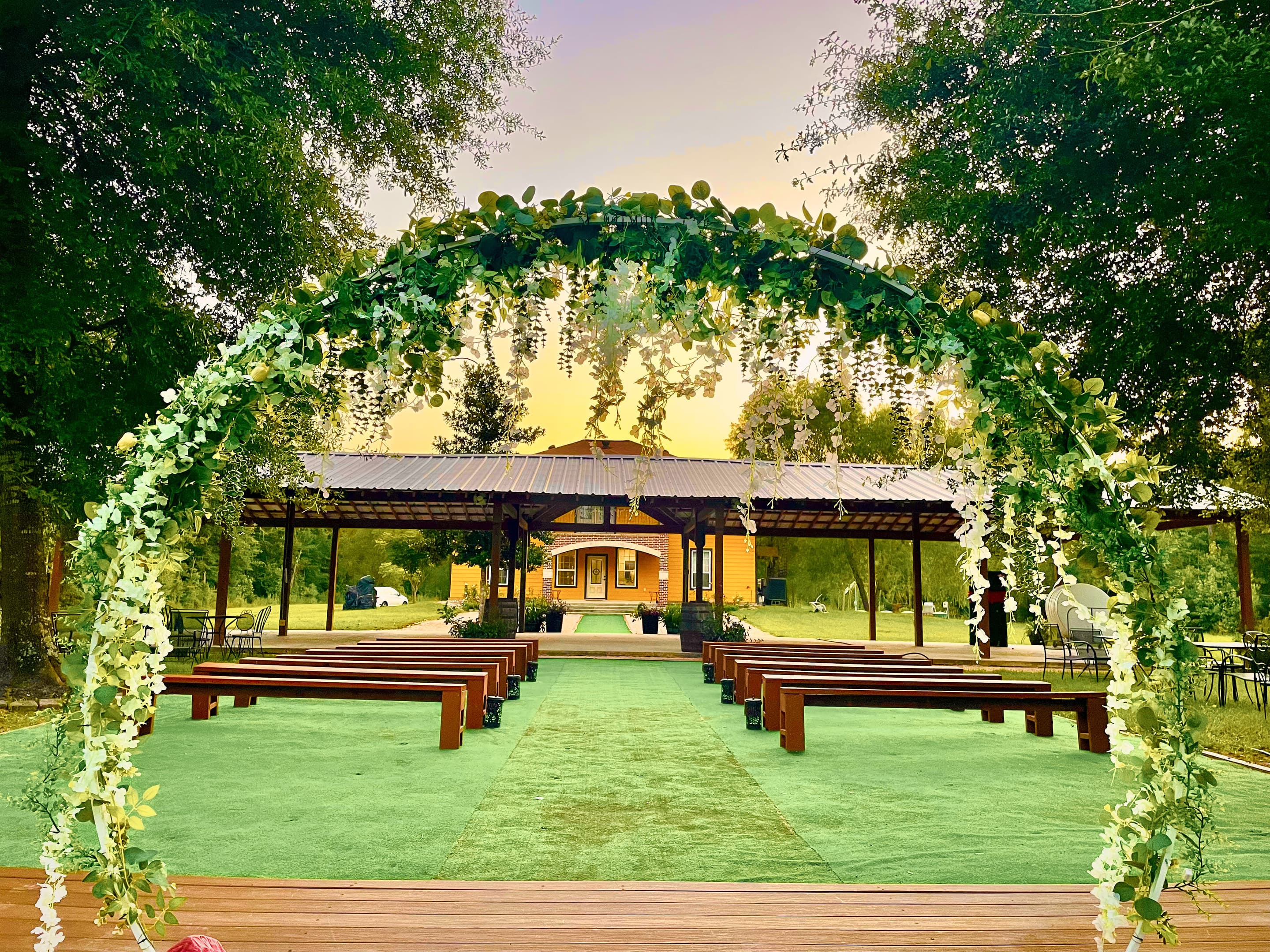 A greenery-draped arch framing the ceremony benches and the timber pavilion at dusk