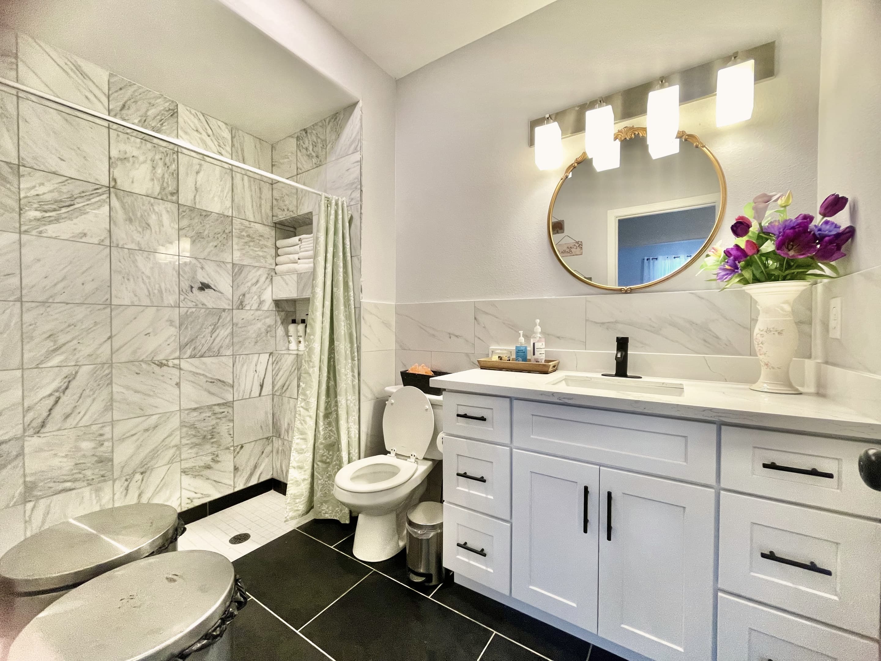 A full bathroom with a marble-look shower, vanity and round mirror