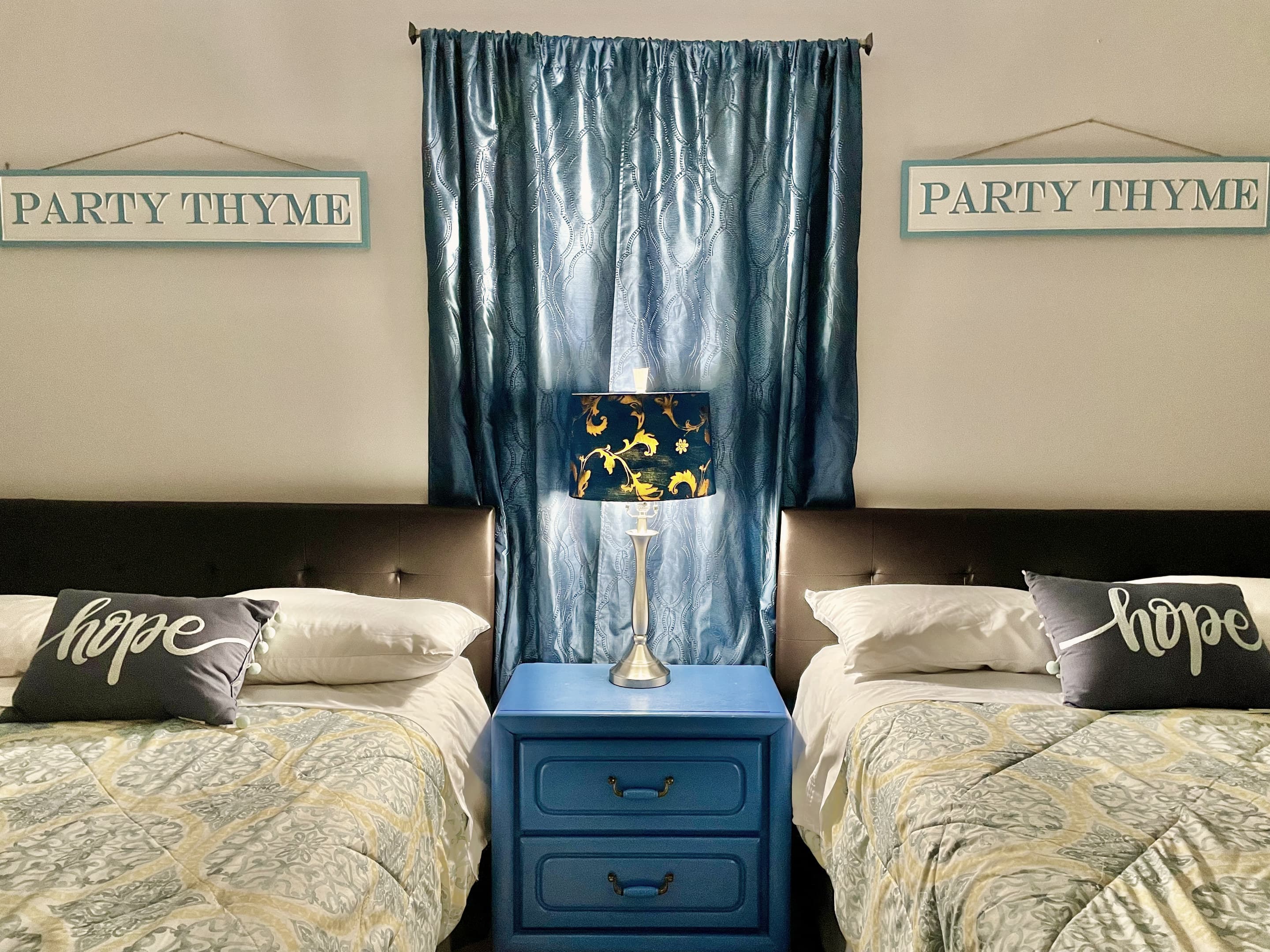 A bedroom with two beds, blue curtains and a matching bedside table