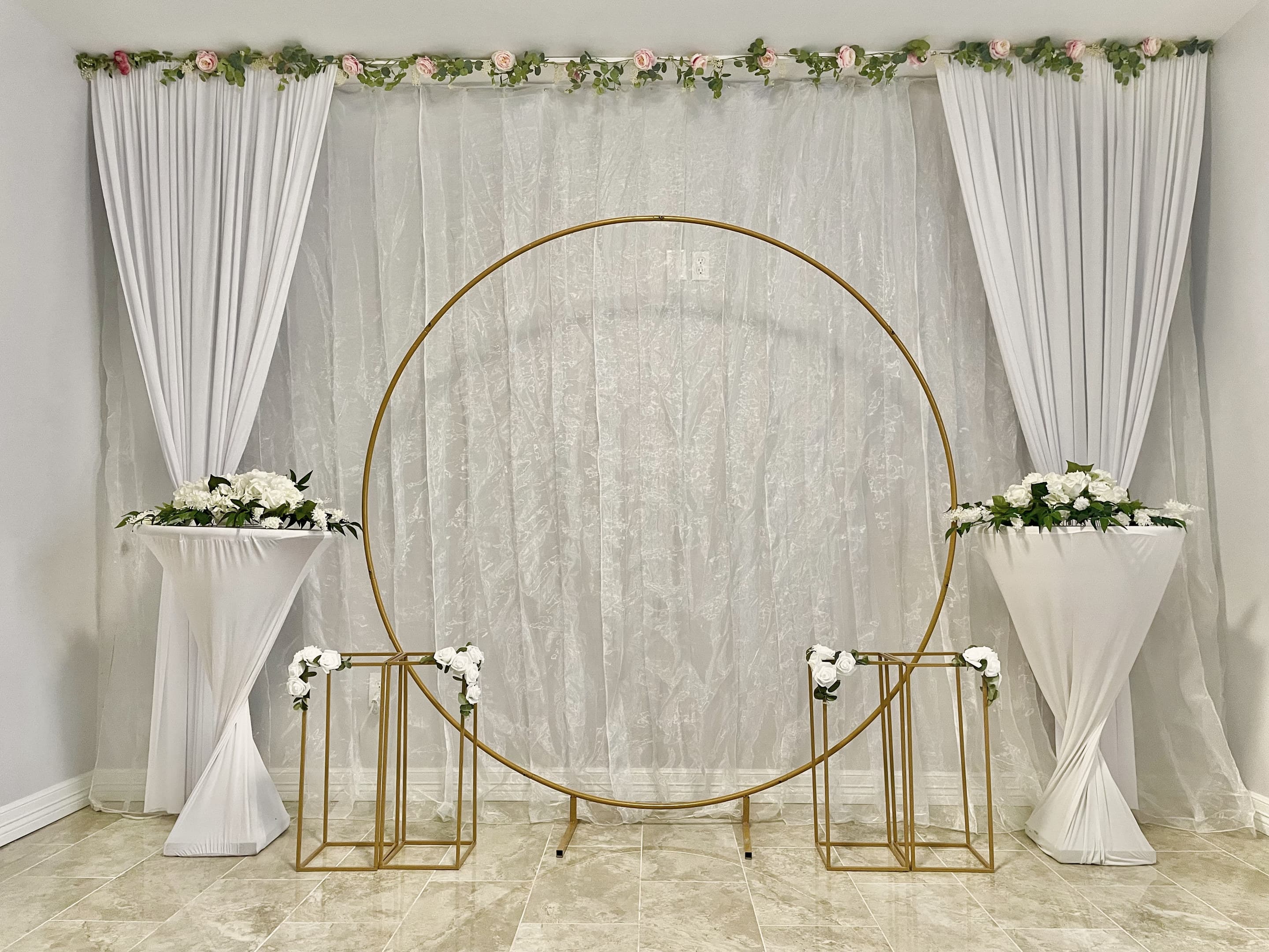 A gold circular ceremony arch with white drapes and floral stands