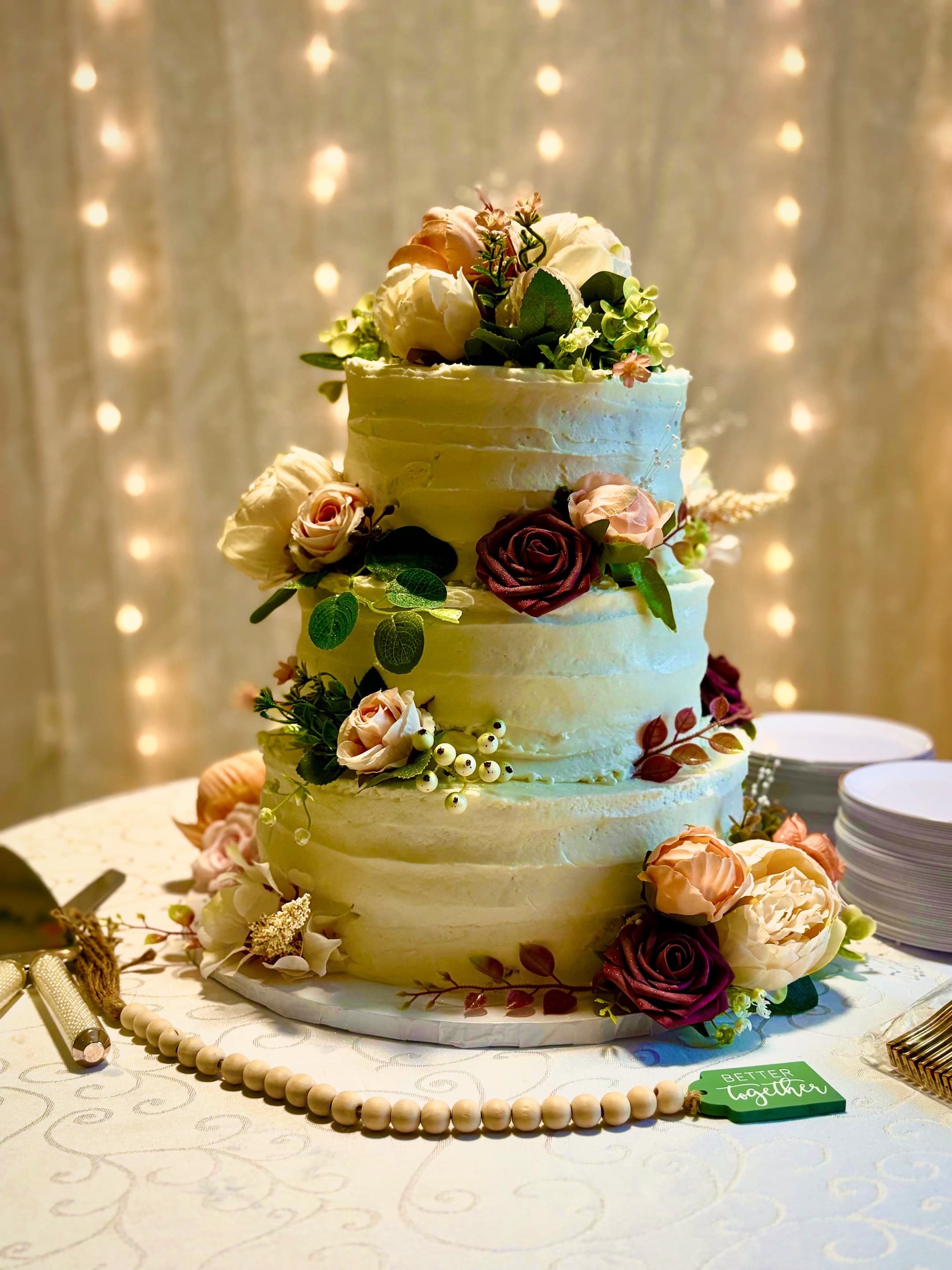 A three-tier buttercream cake decorated with blush and burgundy roses