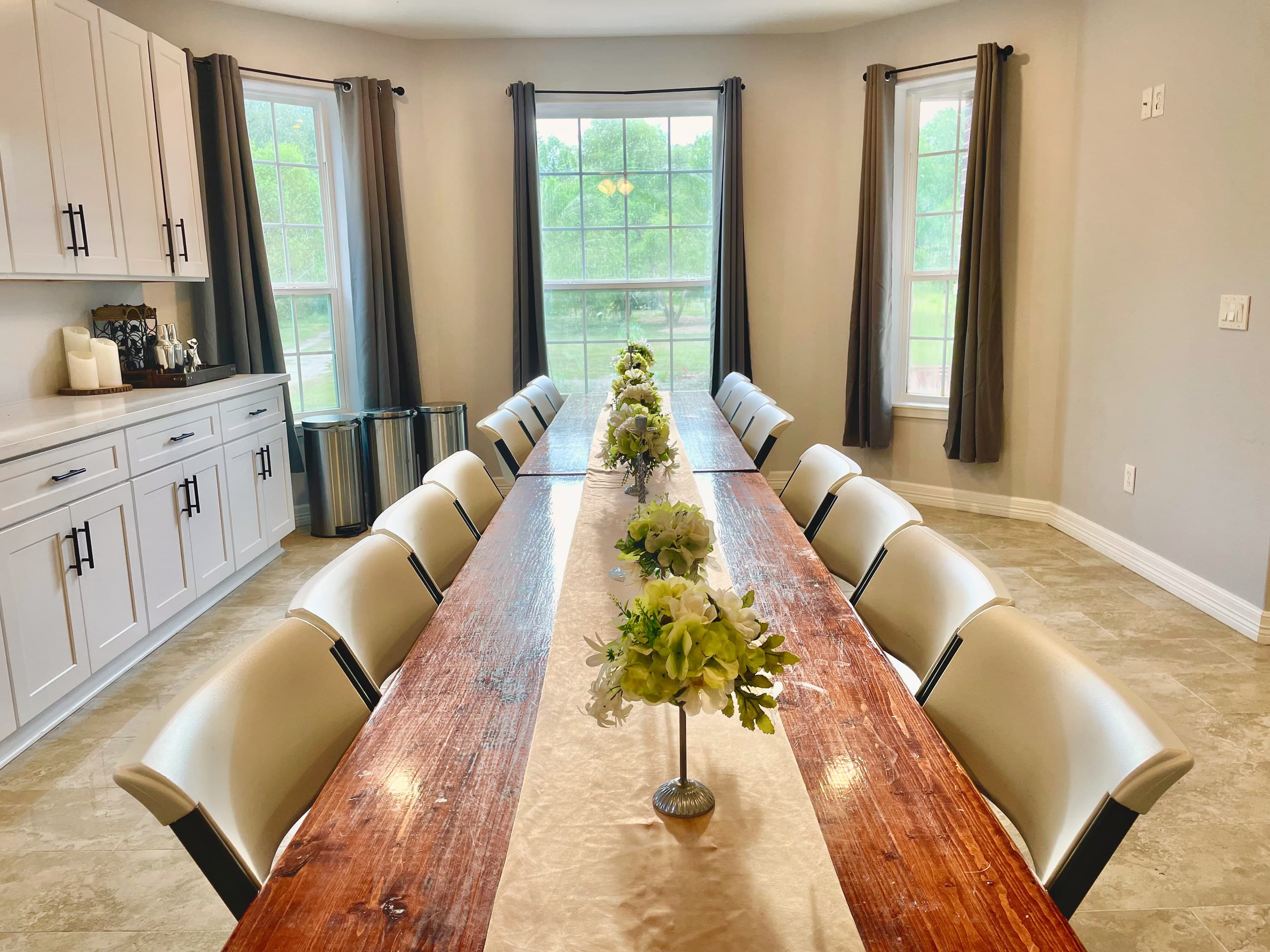 A walnut dining table for twenty with small topiary centrepieces beneath tall windows