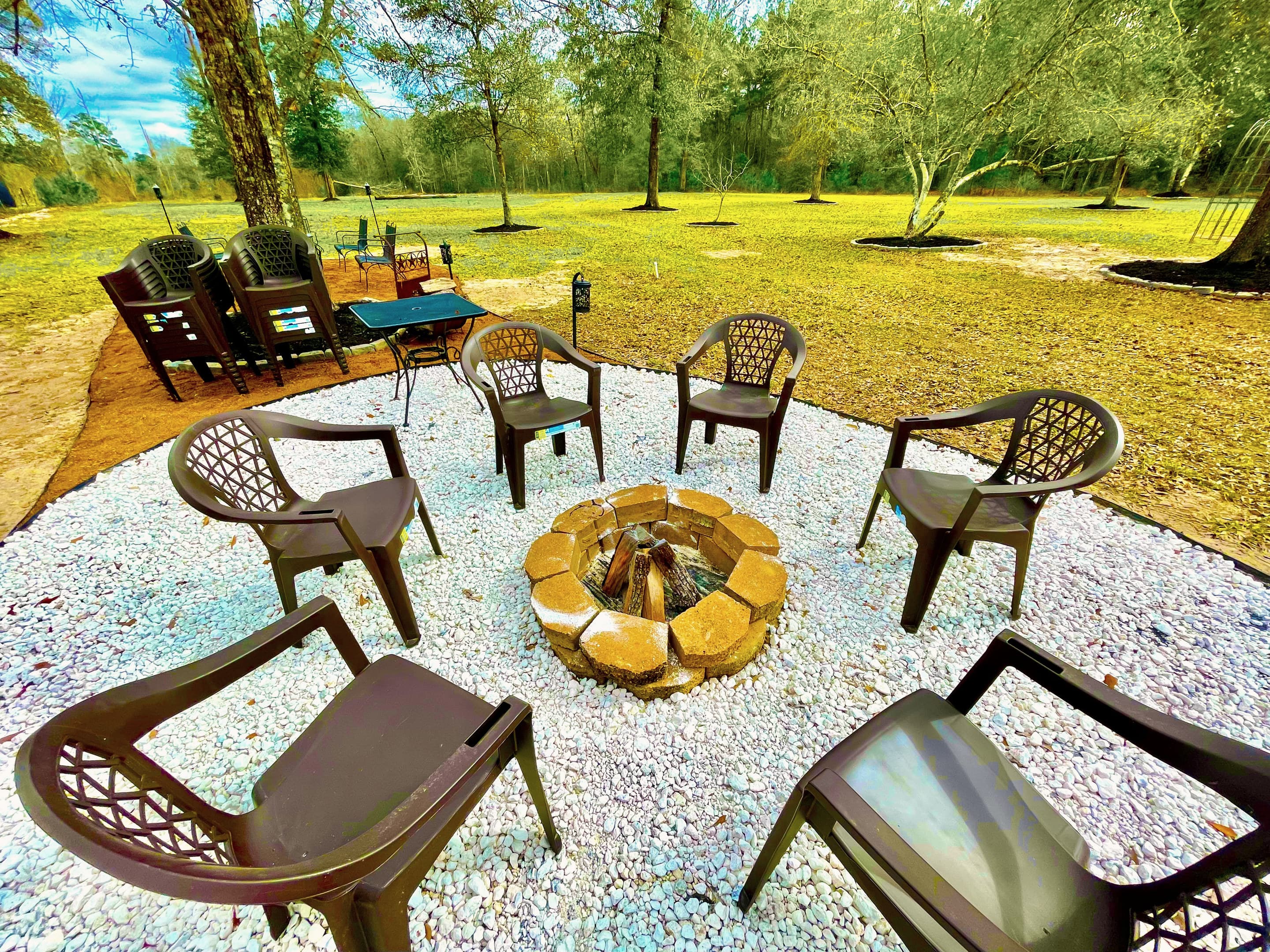 Chairs gathered around the stone fire pit on a gravel circle beneath the trees