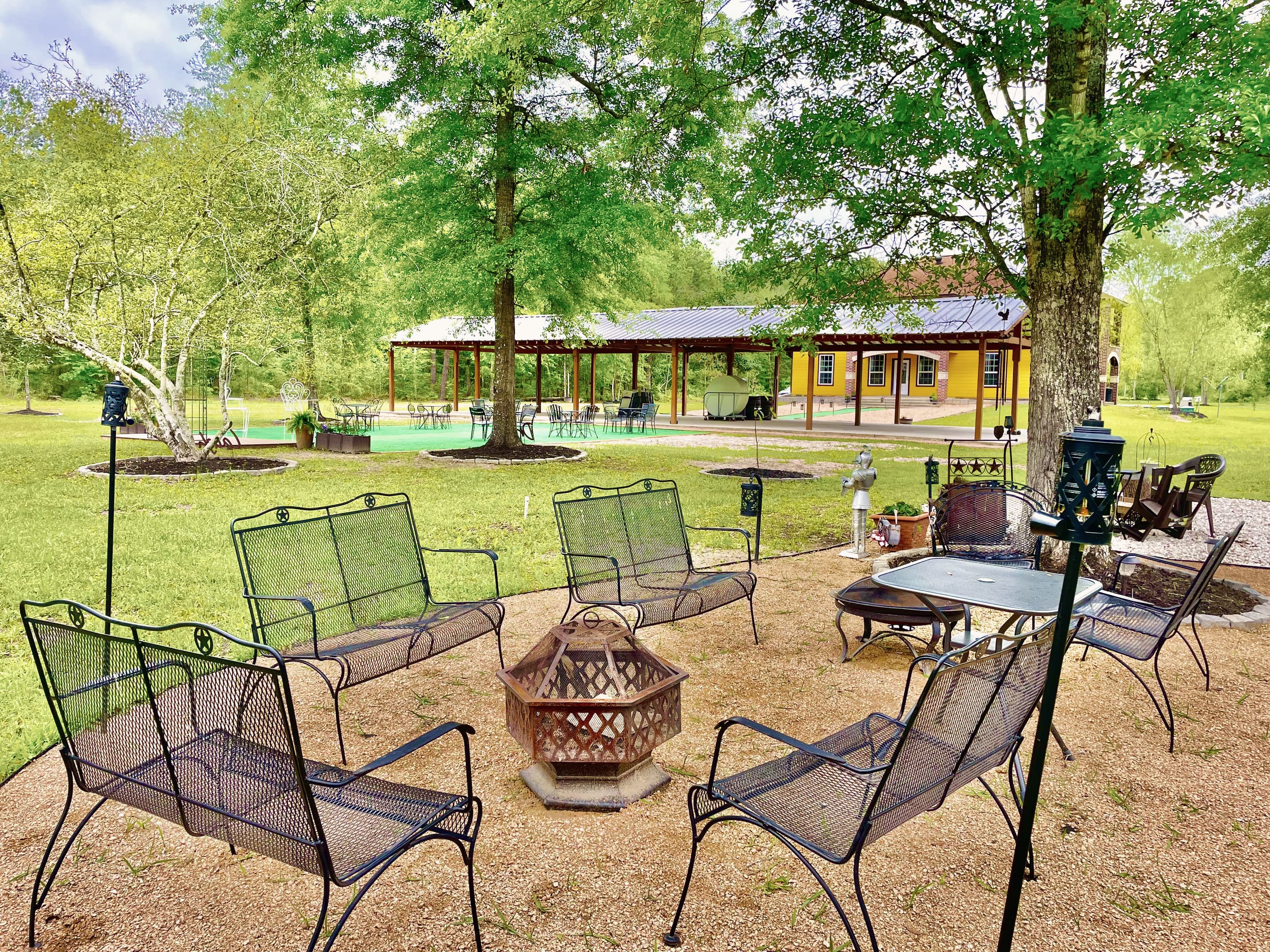 Iron lounge chairs around a fire bowl on the lawn near the pavilion