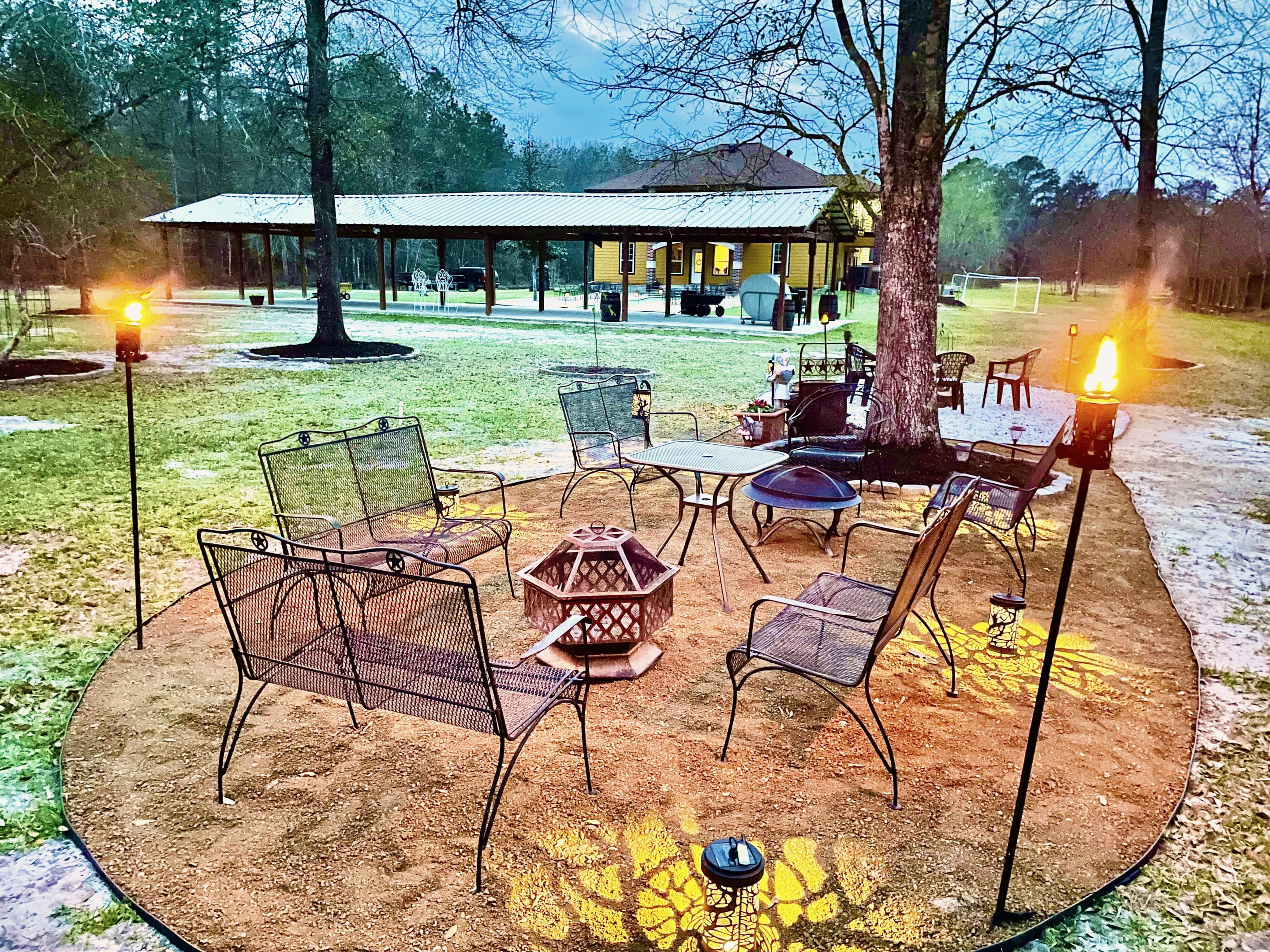 A fire pit ringed by iron chairs and tiki torches, the pavilion in the distance