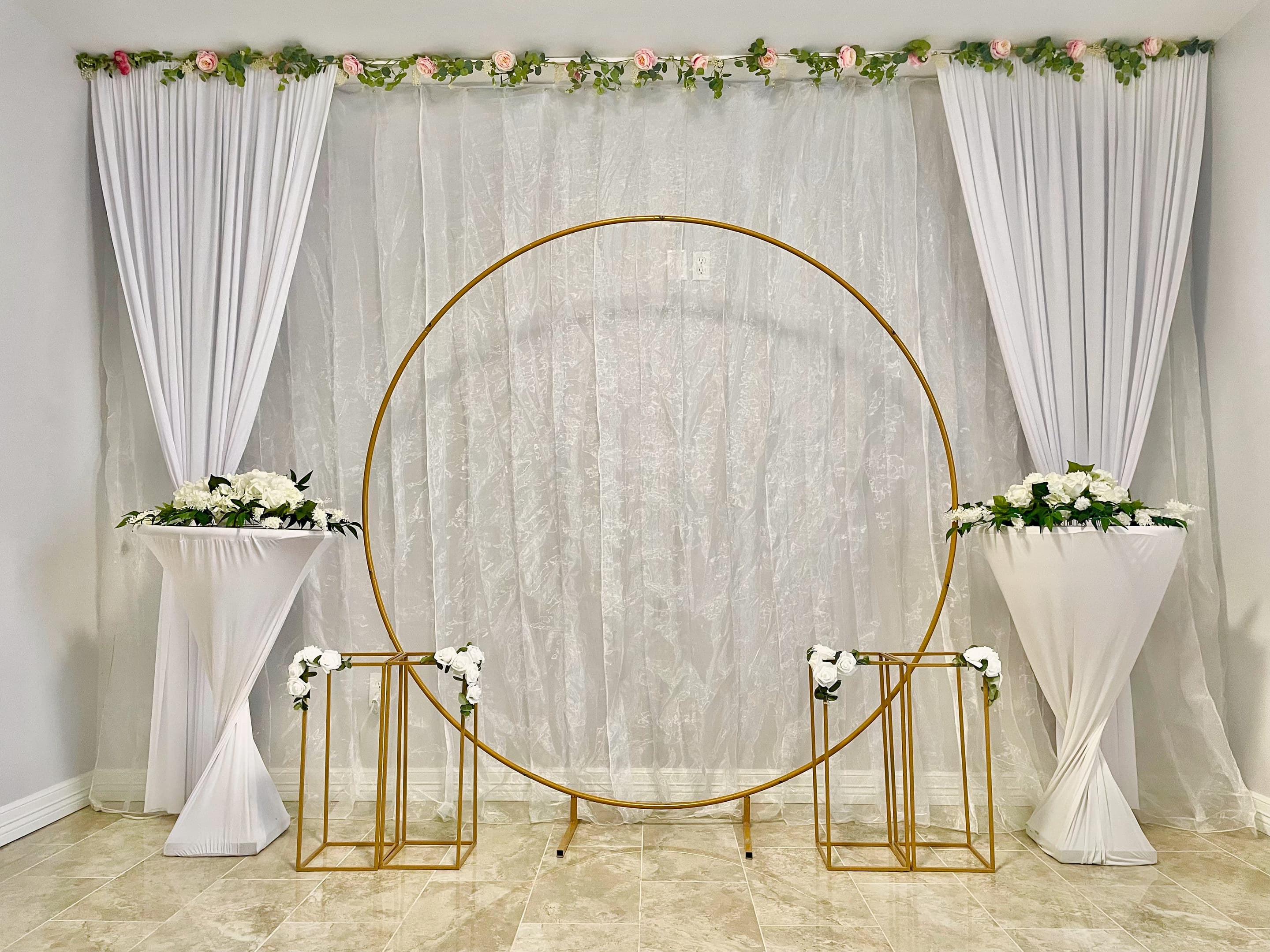 A gold circular arch framed by ivory drapery and flower-topped pedestals for an indoor ceremony