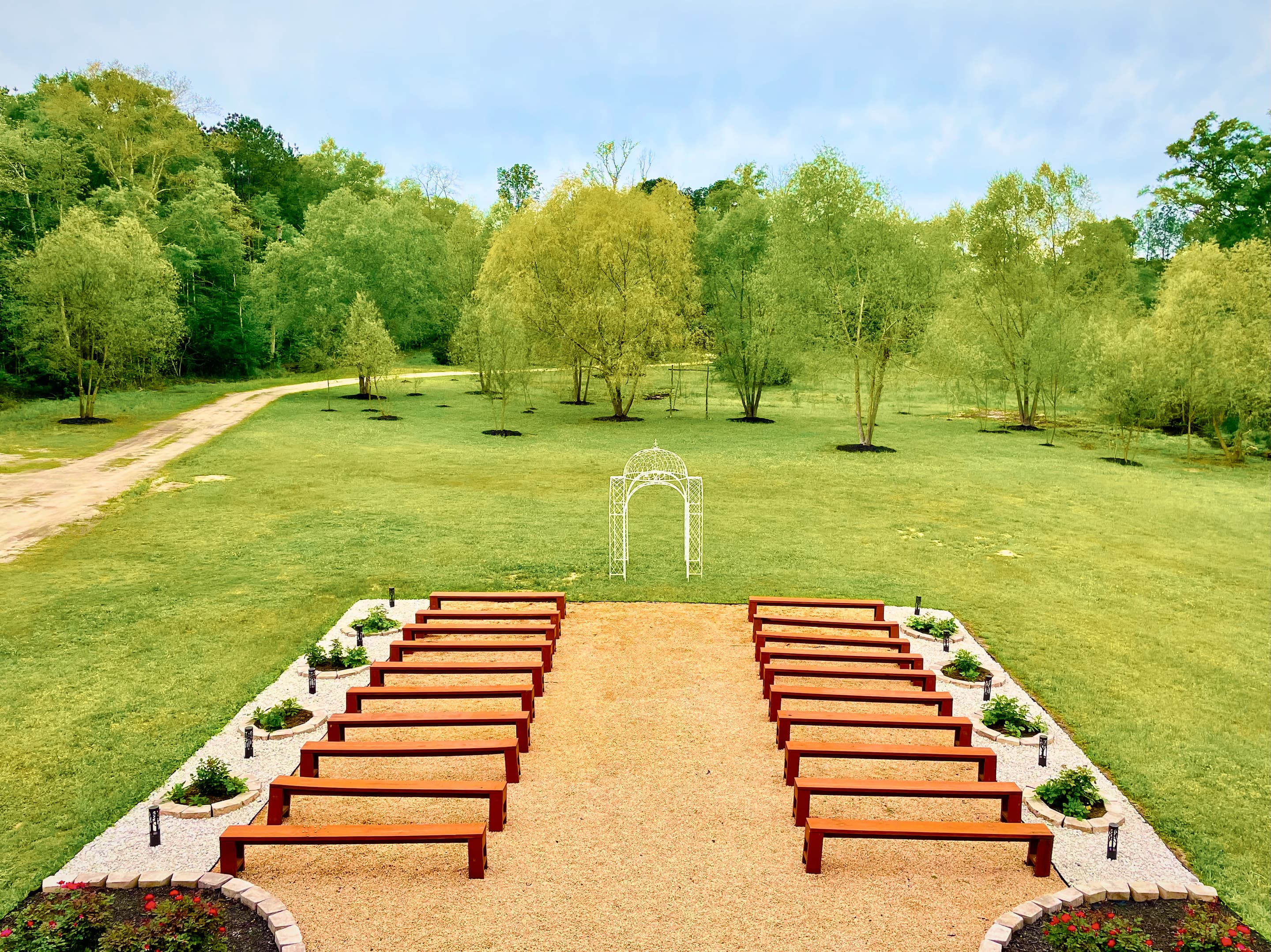 A gravel ceremony aisle edged in white stone, leading to a garden arch on the open lawn