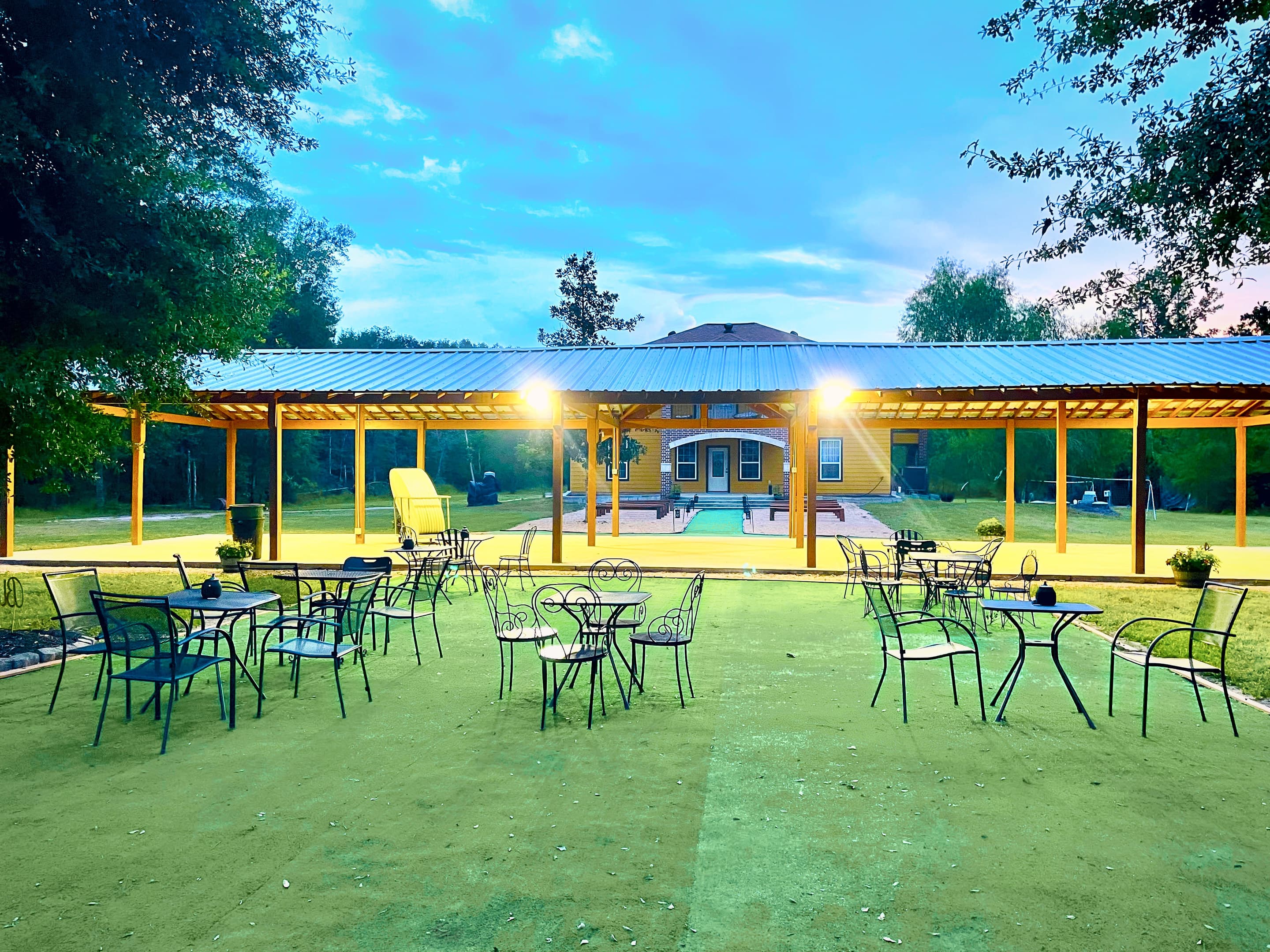Bistro tables on the lawn before the lit pavilion at dusk
