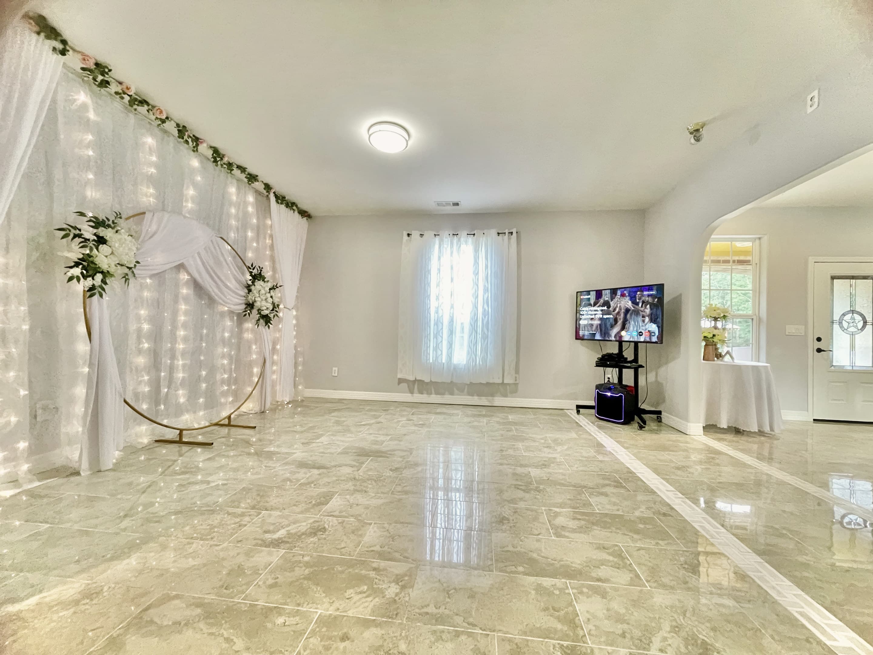 The manor's open party room with marble-look floors, fairy-light drapes and a gold arch