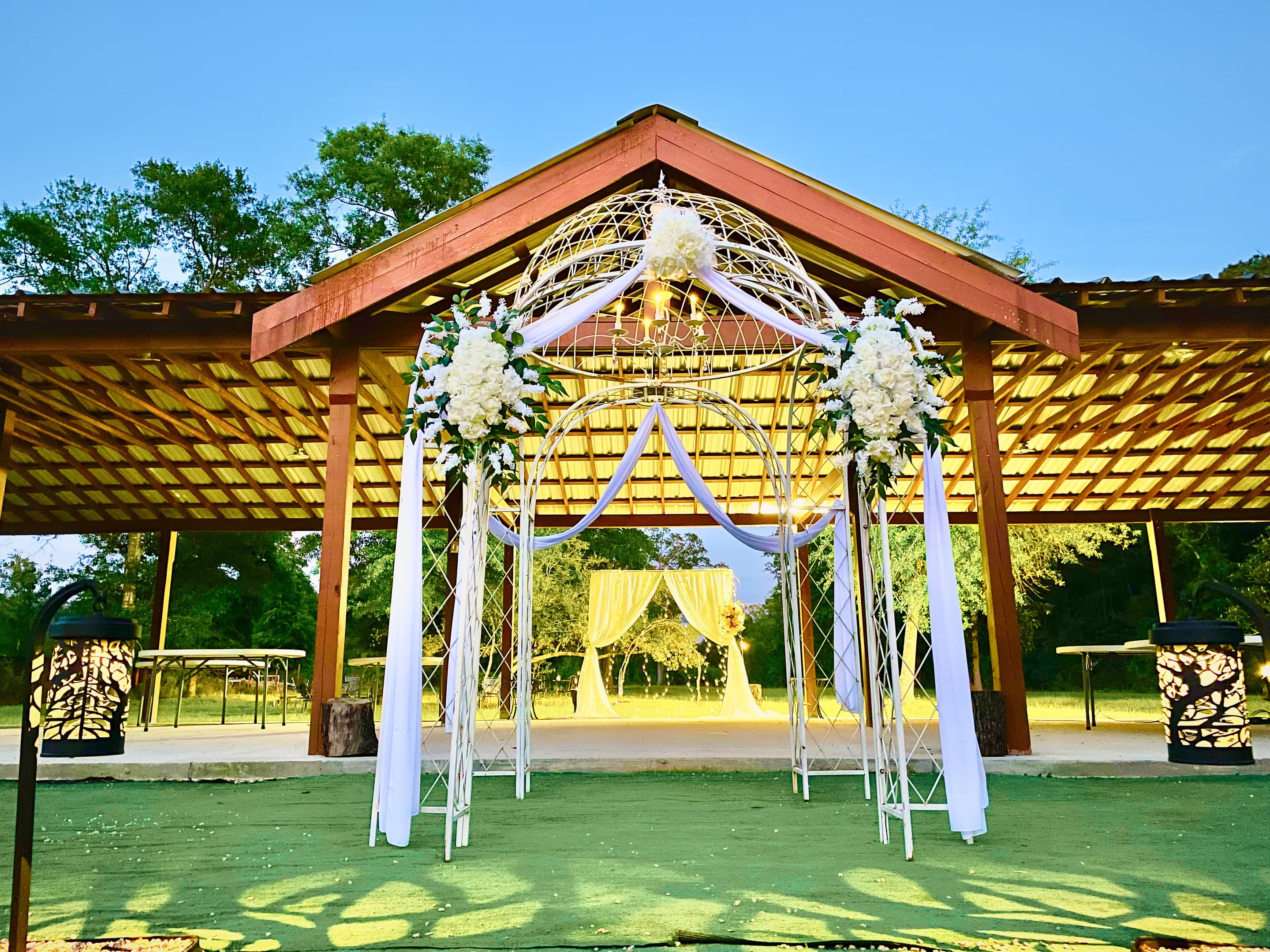 A white floral arch dressed in ivory blooms and drapery beneath the pavilion gable