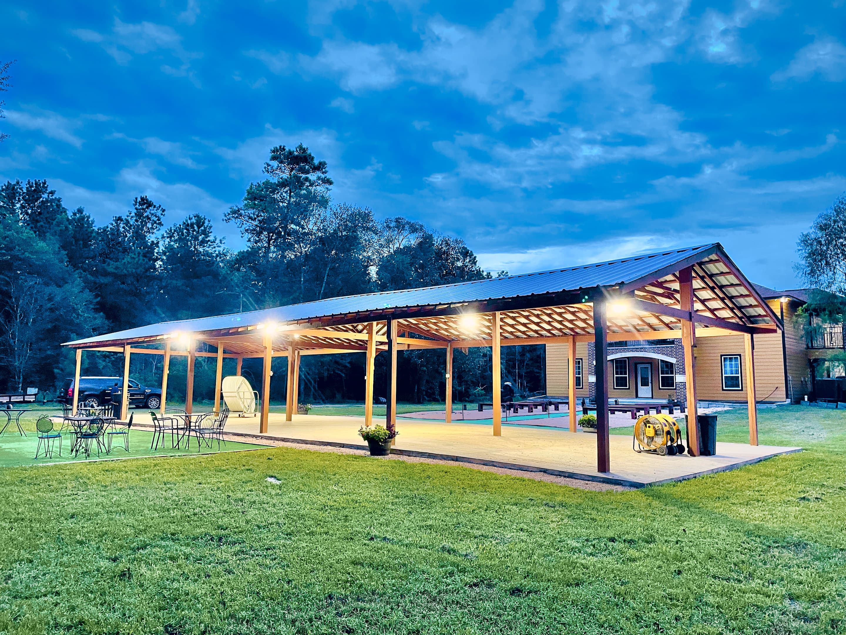The open-sided pavilion glowing with warm light across the lawn at dusk