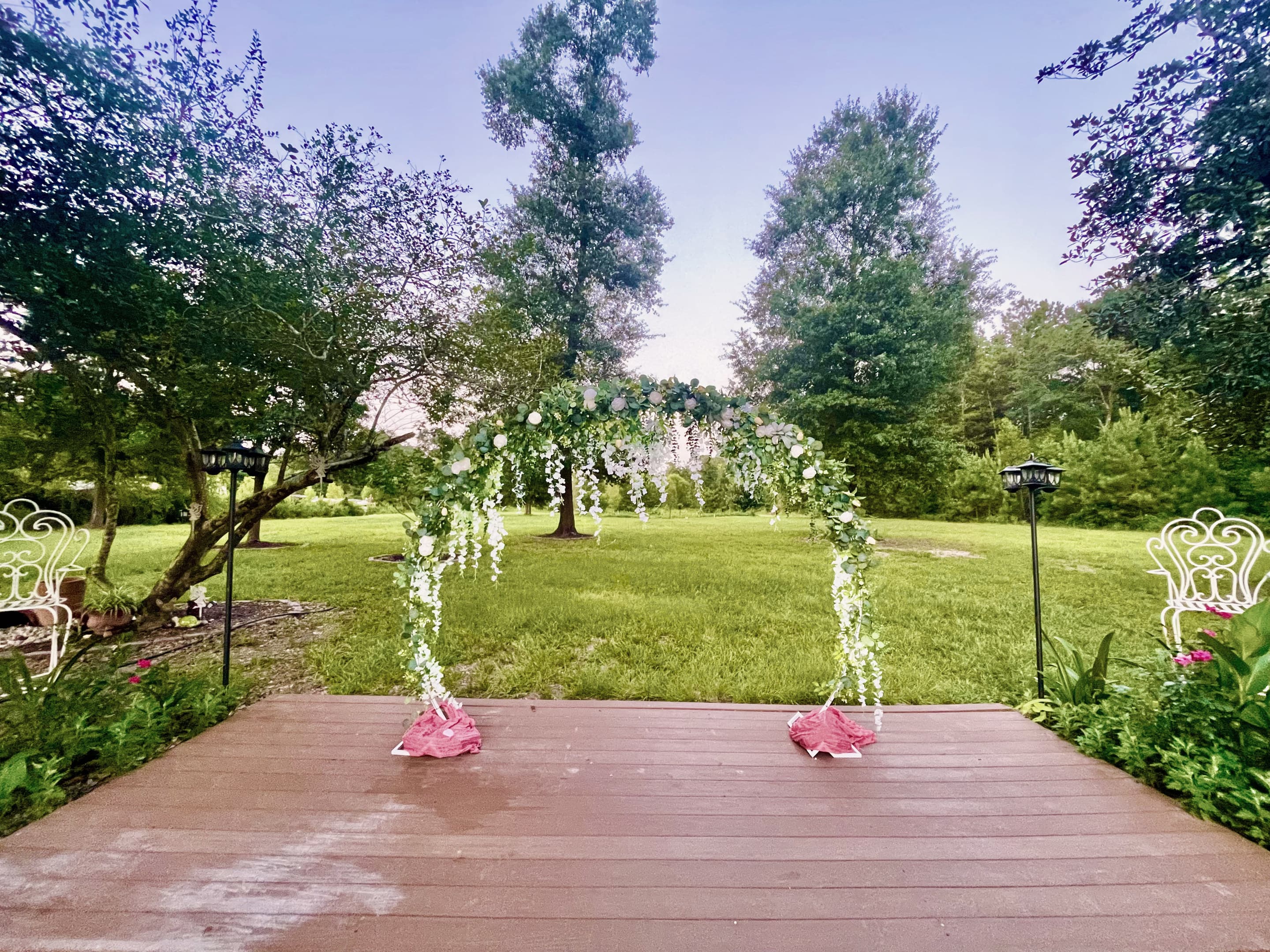Petals across the timber stage between two floral arches, the lawn beyond
