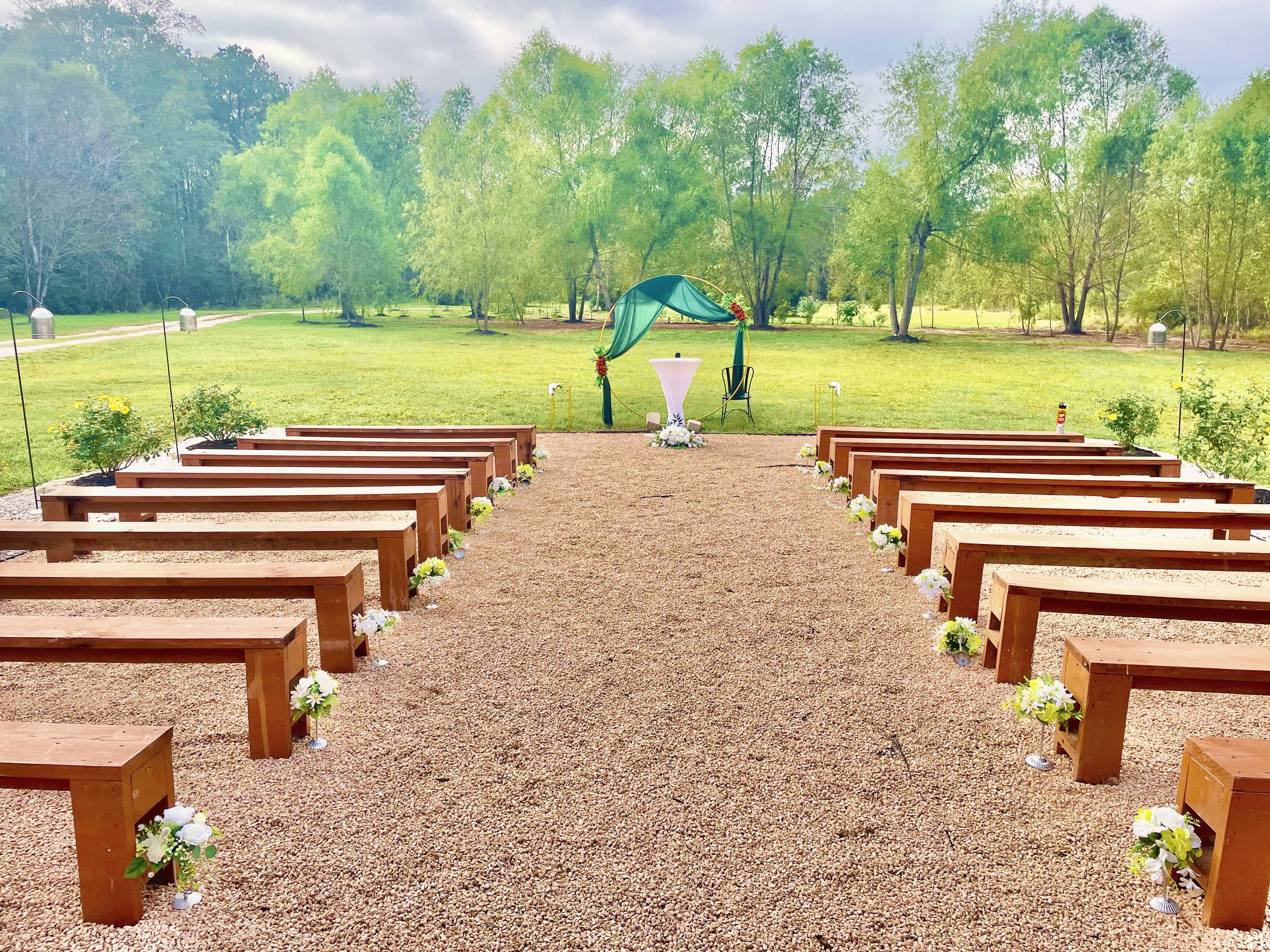 Timber benches along a gravel aisle leading to a garden arch beside the willow trees