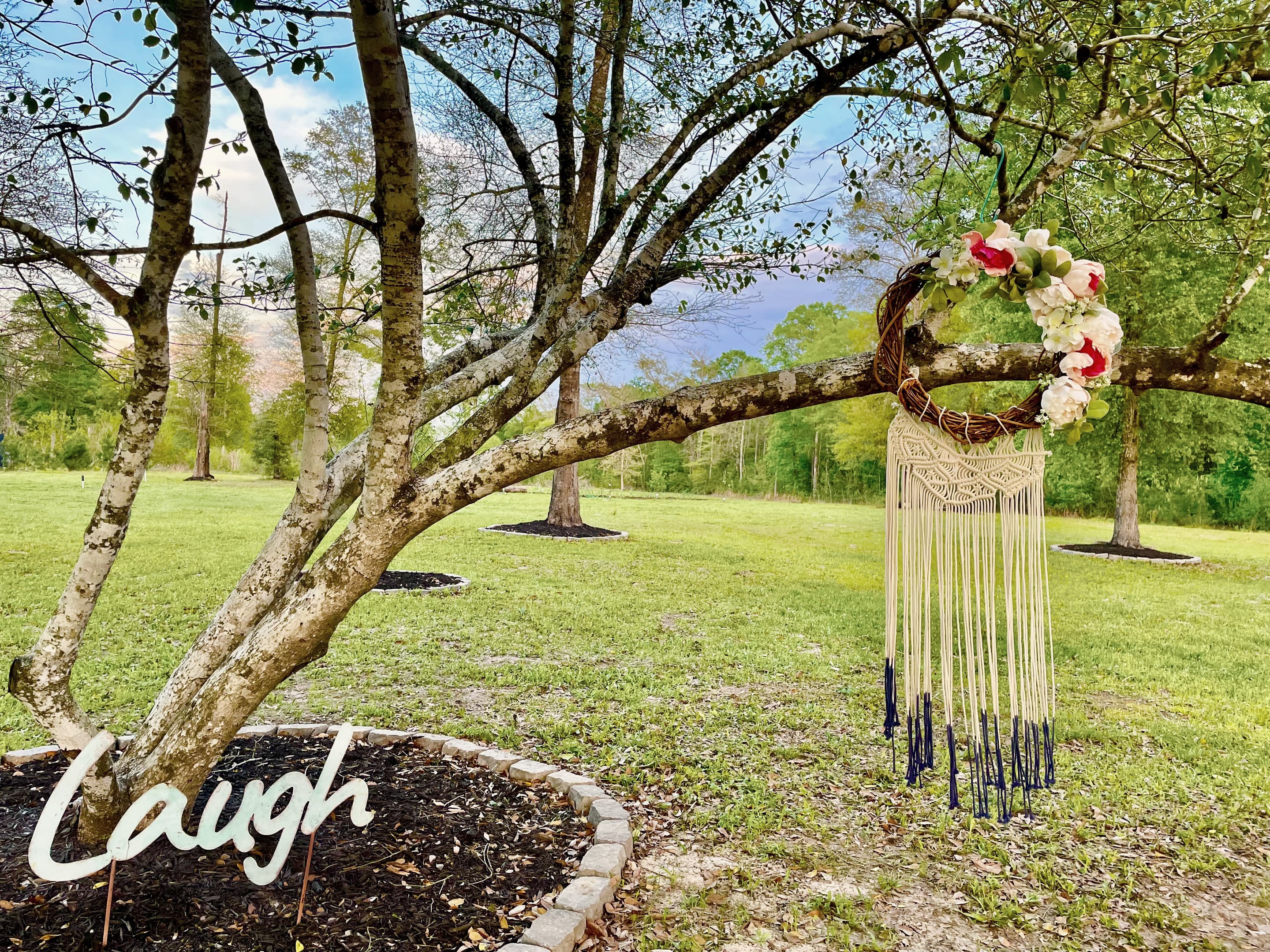 A macrame hanging and a 'Laugh' sign beneath a spreading tree in the backyard